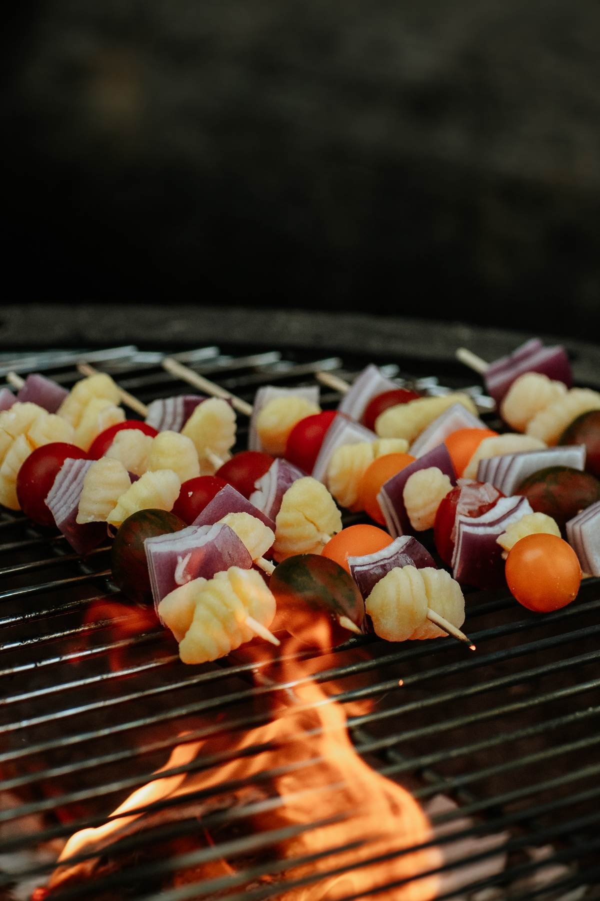 Campfire Gnocchi Kebabs and vegetable and cheese skewers grilling over an open flame on a barbecue grill.