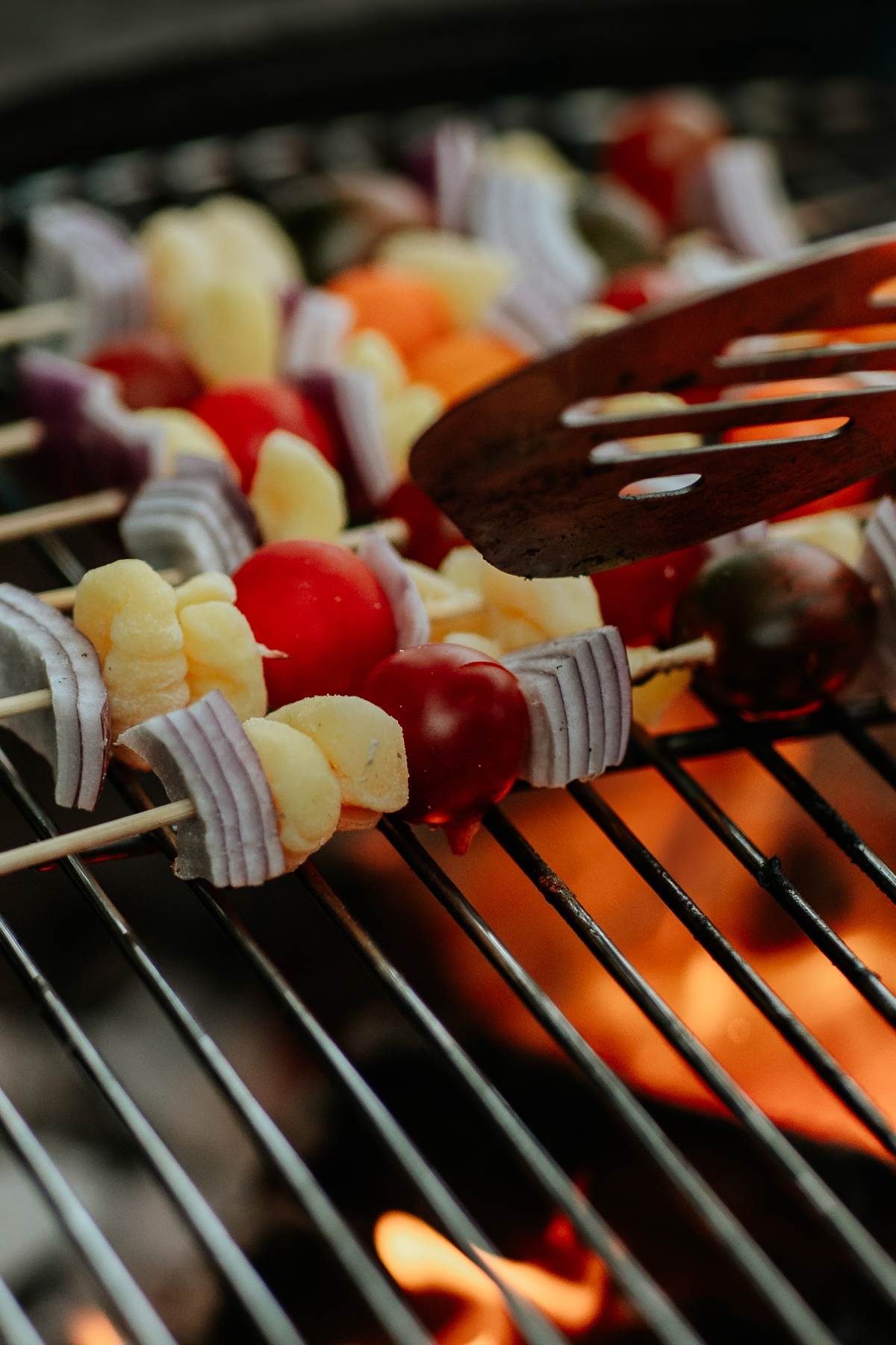 Vegetable skewers with tomatoes, onions, and cauliflower grilling over an open flame on a barbecue grill&mdash;perfect alongside Campfire Gnocchi Kebabs for a delicious outdoor feast.