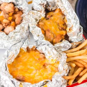 Enjoy our Campfire Chicken Foil Packs—four foil packets filled with cheesy chicken and vegetables, served alongside crispy French fries.