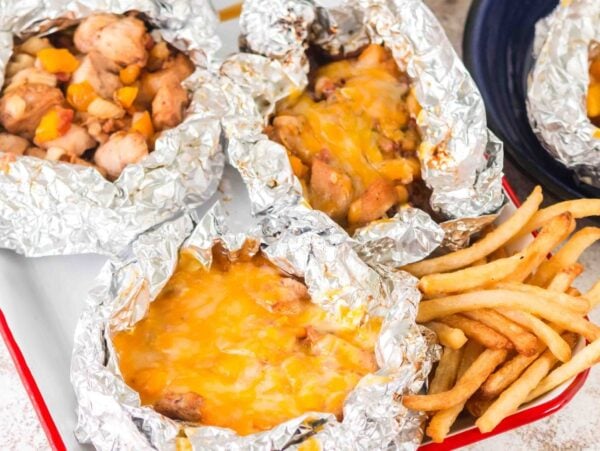 Enjoy our Campfire Chicken Foil Packs—four foil packets filled with cheesy chicken and vegetables, served alongside crispy French fries.