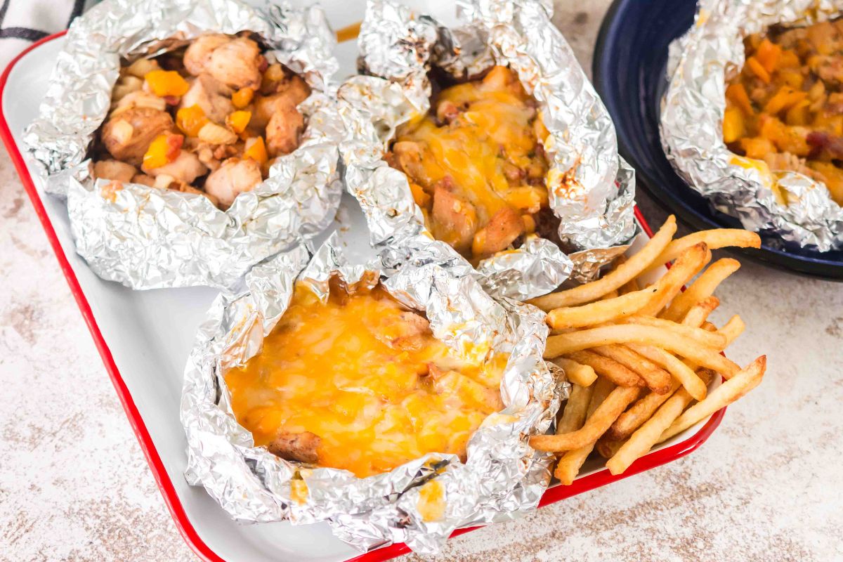Campfire Chicken Foil Packs: Three foil packets with cheesy chicken and veggies, served on a tray with a side of French fries.