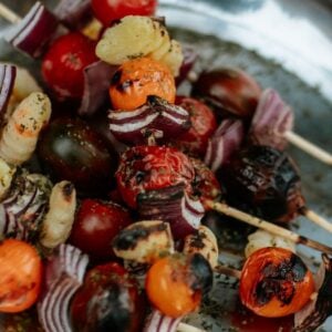 Campfire Gnocchi Kebabs feature grilled vegetable skewers with tomatoes, onions, and gnocchi, all served on a metal plate.