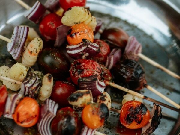 Campfire Gnocchi Kebabs feature grilled vegetable skewers with tomatoes, onions, and gnocchi, all served on a metal plate.