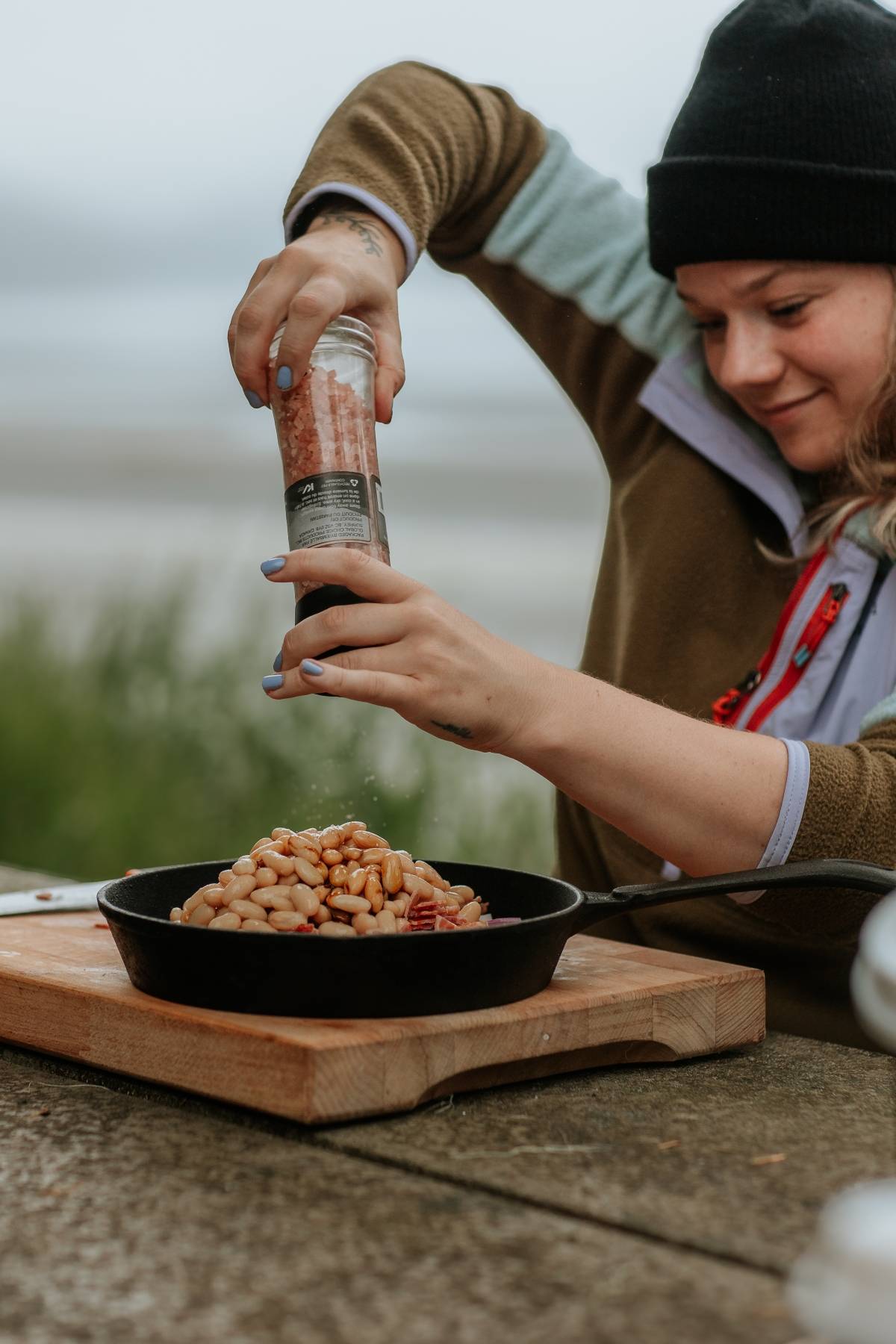 A person grinds pepper onto white beans in a cast iron skillet outdoors.