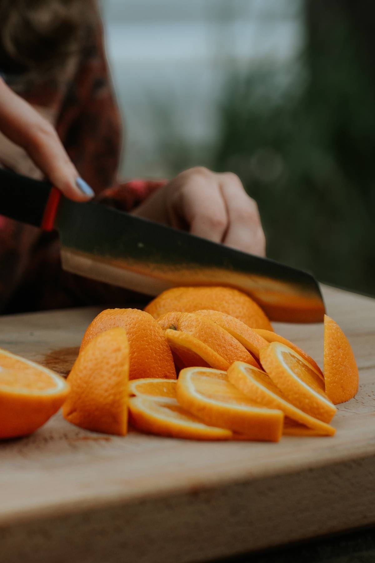 A person slicing an orange into thin pieces on a wooden cutting board.
