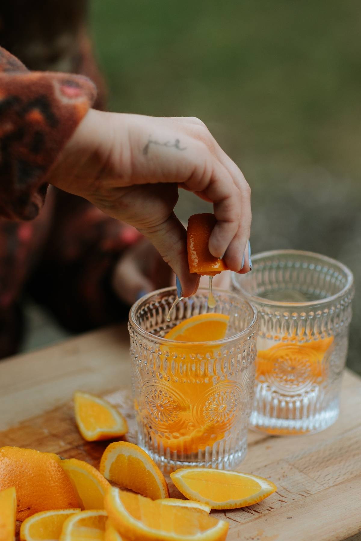 A hand squeezes an orange slice into a glass with more orange slices on a wooden board.