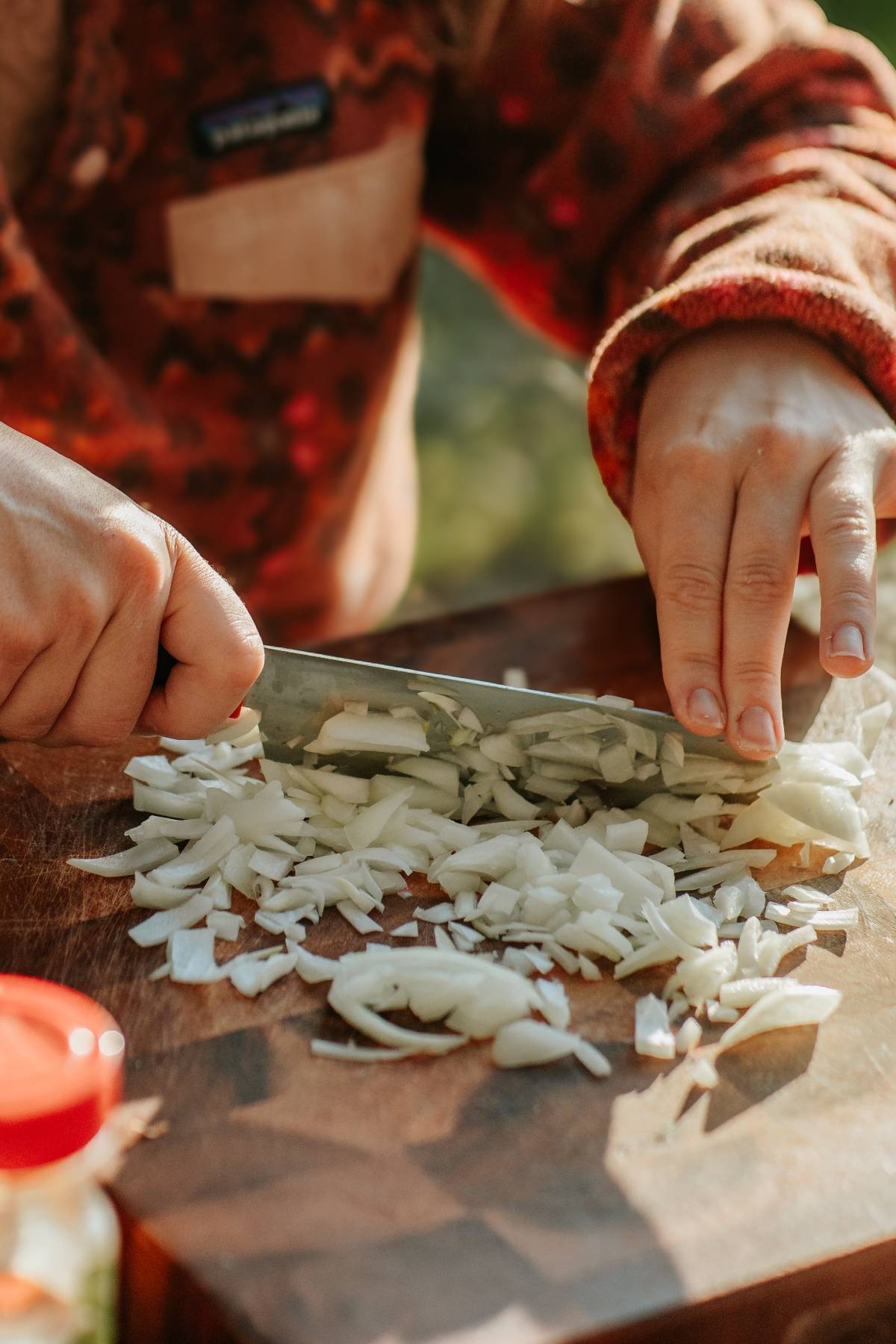 A person chopping white onions on a wooden cutting board with a knife.