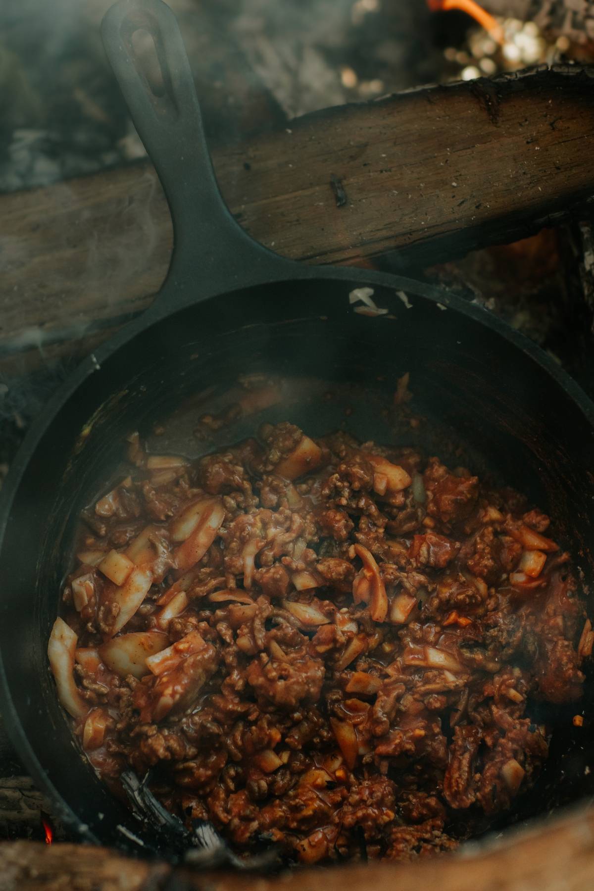 A cast iron skillet with cooked ground meat and onions over an open fire.