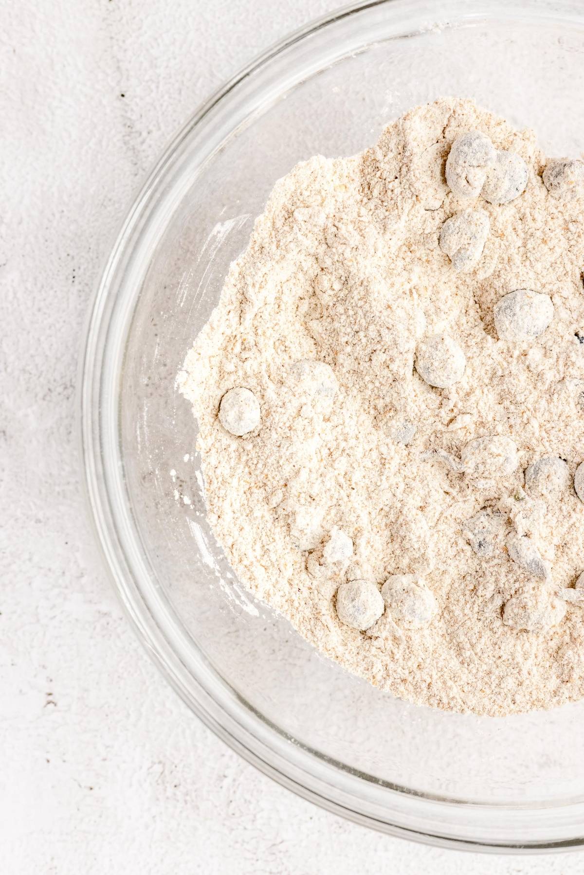 A glass bowl with flour and chocolate chips on a white surface, perfect for starting your carrot blueberry muffins or any carrot and blueberry recipe.
