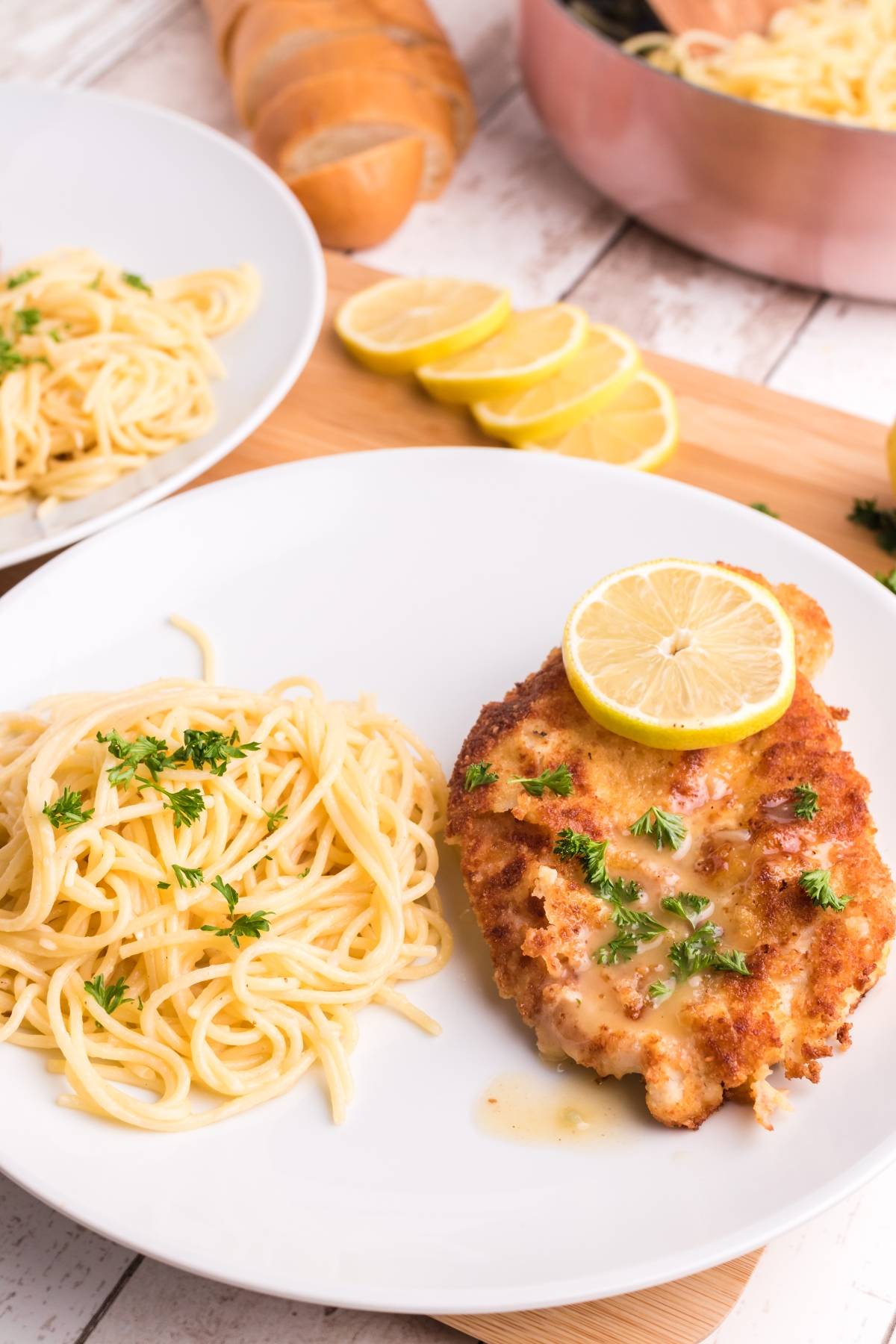 A plate of Chicken Scallopini with Lemon Sauce served alongside angel hair pasta and parsley garnish on a white plate.