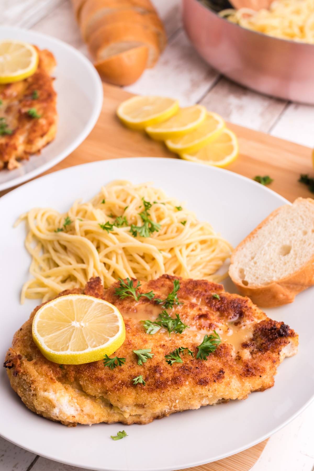 Breaded chicken cutlet with lemon slice, angel hair pasta, and bread on a white plate, garnished with parsley—an easy chicken and pasta meal perfect for any night.