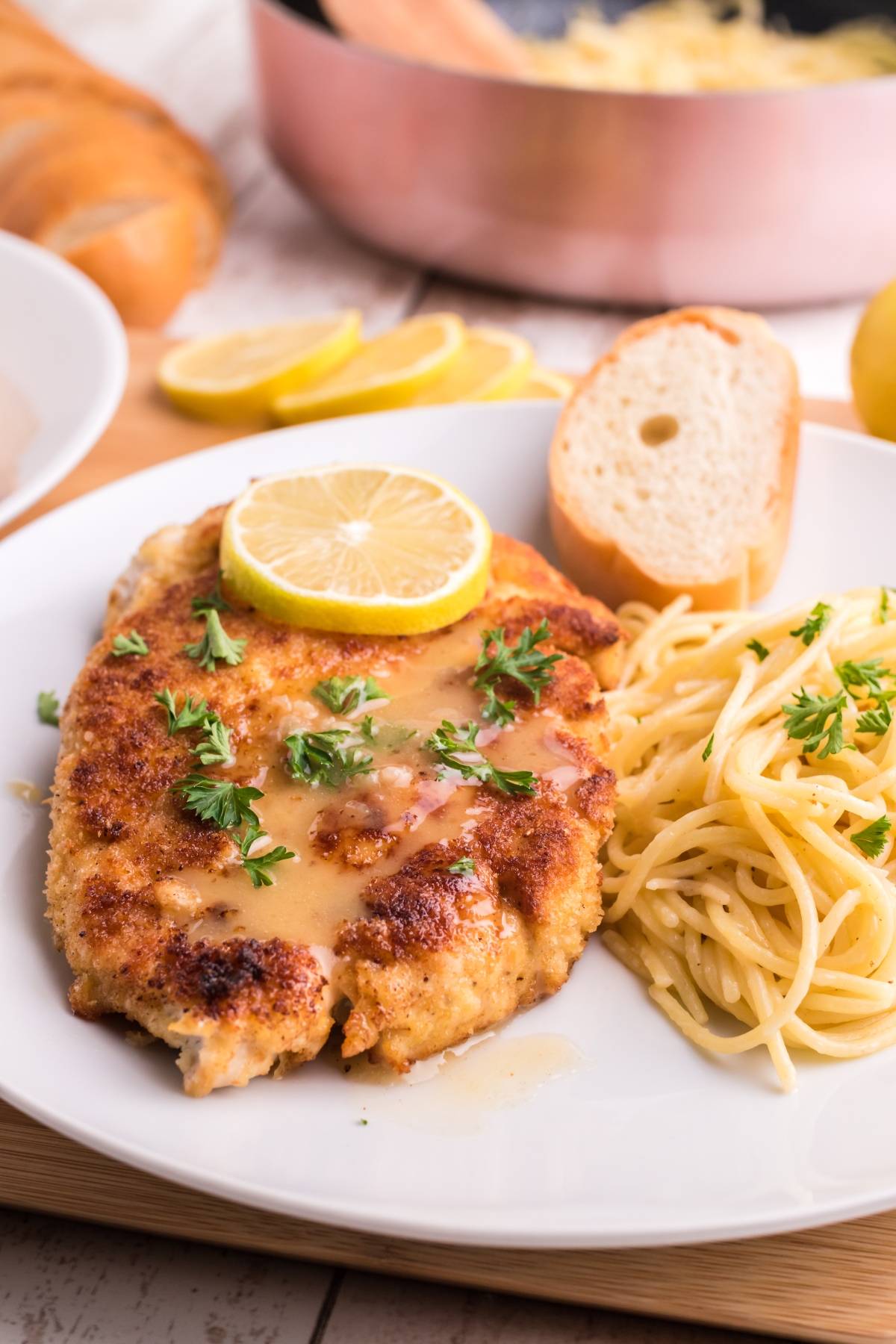 A plate with gluten free Chicken piccata, lemon slice, angel hair pasta, bread, and a parsley garnish.