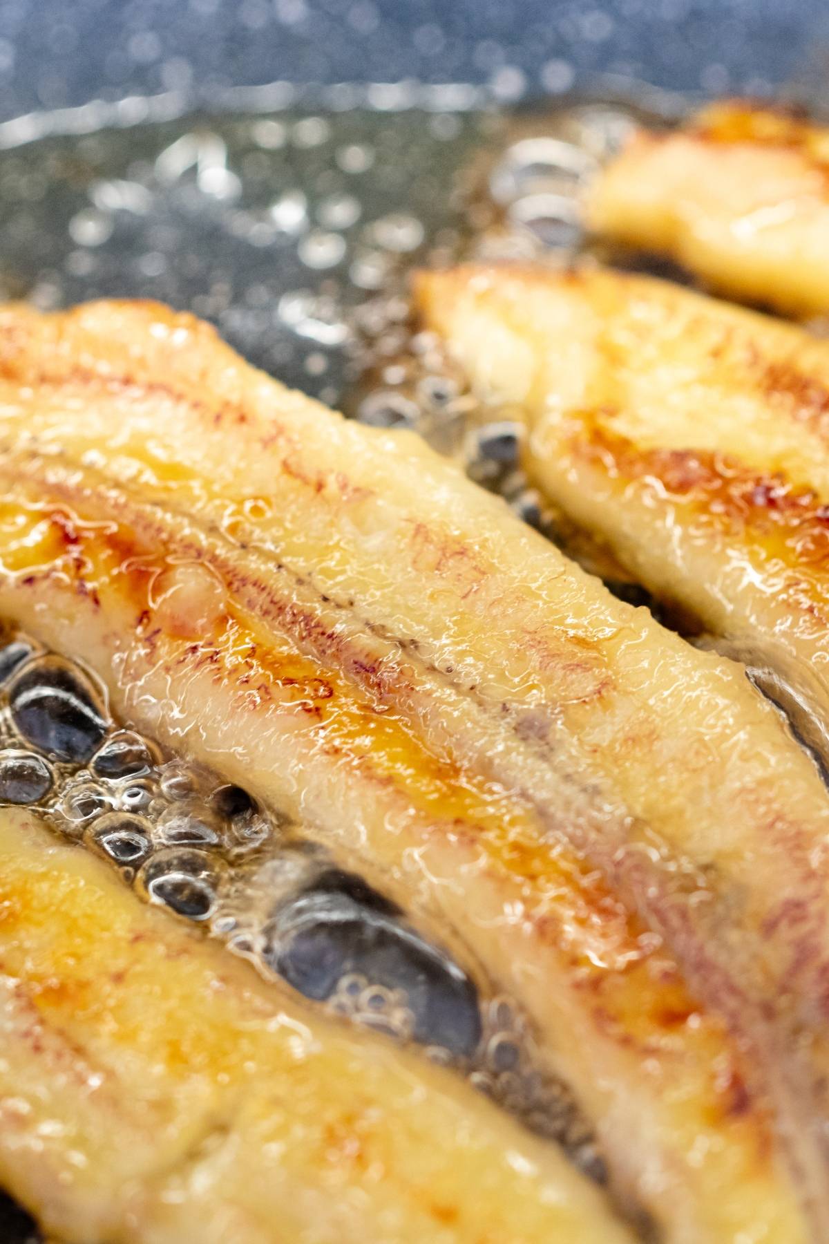 Sizzling strips of bacon frying in hot oil on a pan, perfect to pair with a gluten free pancake for a savory breakfast.