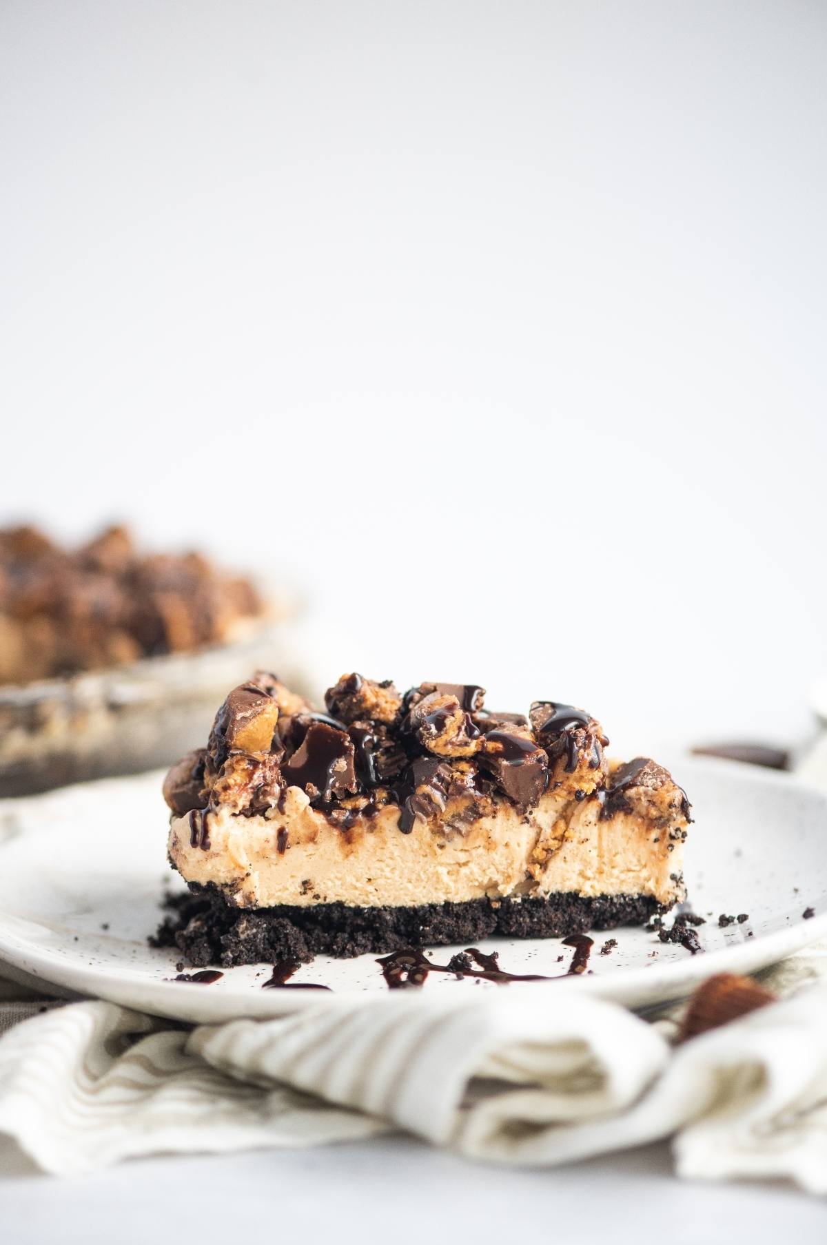 A slice of chocolate peanut butter pie with a rich chocolate graham crust and chocolate drizzle on a white plate.