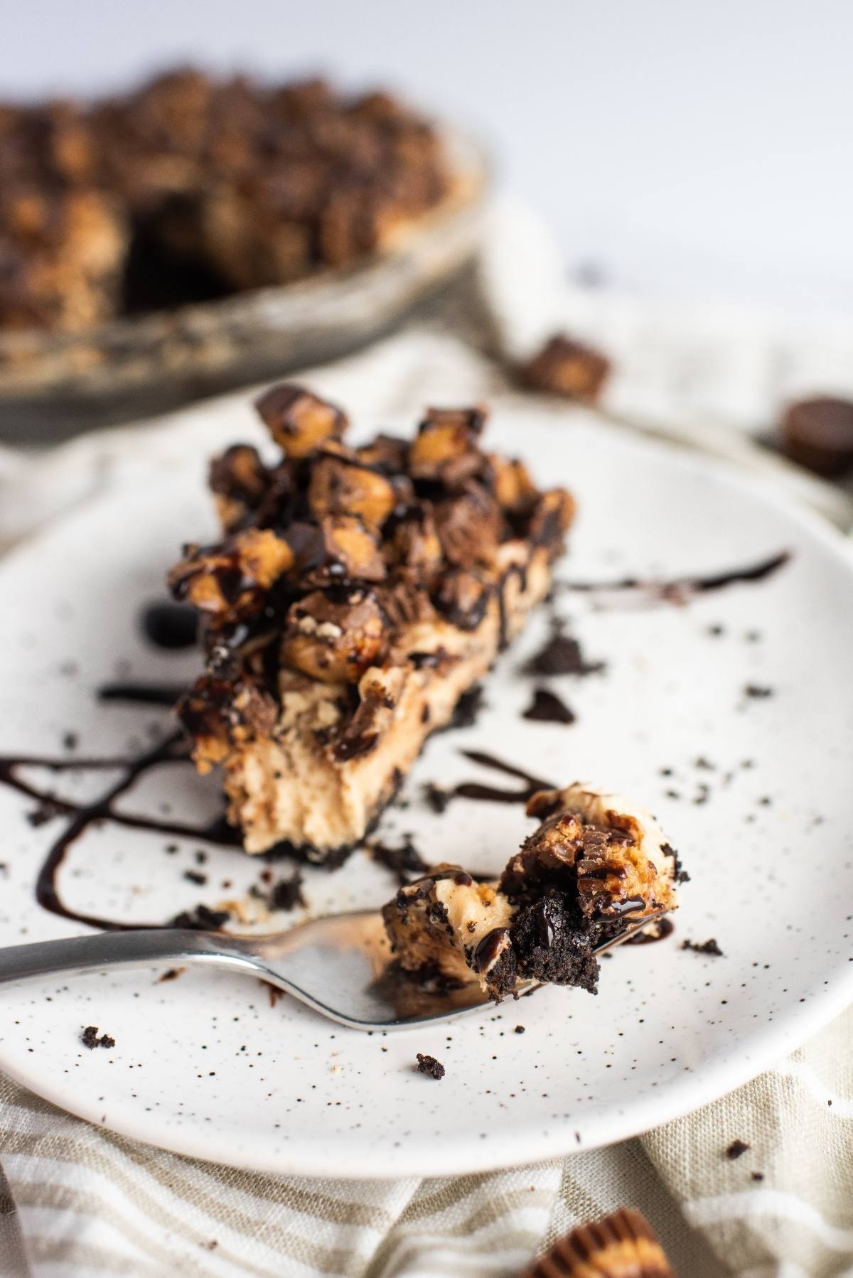 A slice of chocolate peanut butter pie topped with chocolate drizzle and chopped candy sits on a white plate—a decadent recipe with peanut butter cups for the ultimate indulgence.