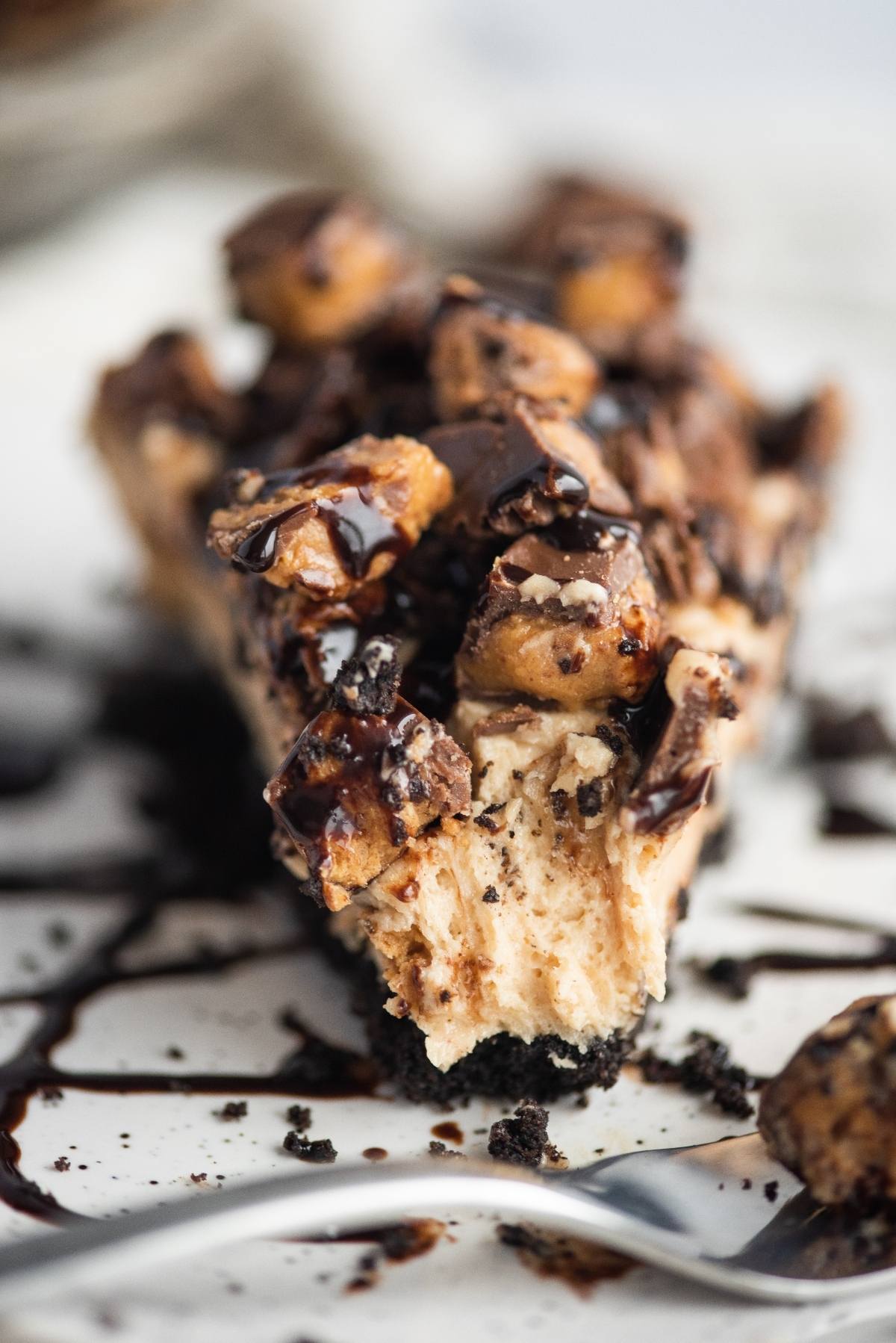 A close-up of a creamy peanut butter cream pie topped with chopped candy pieces and drizzled with chocolate sauce.