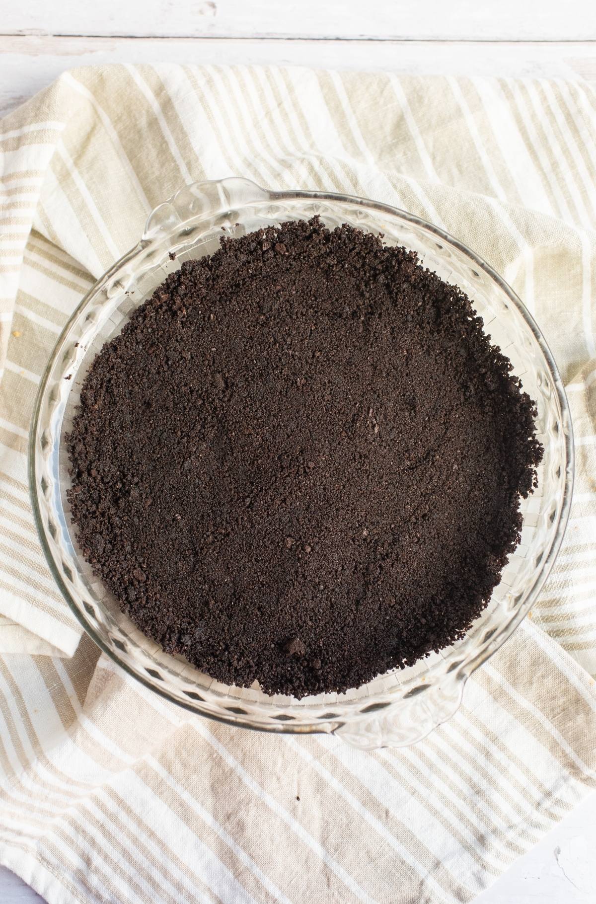 A glass pie dish with a chocolate cookie crumb crust holds a luscious chocolate peanut butter pie, set on a striped cloth.