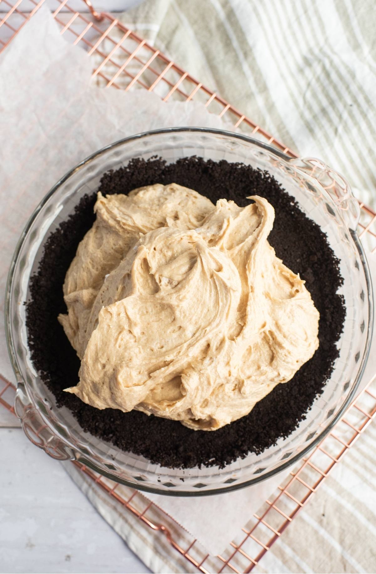 Glass pie dish with cookie crumb crust, filled with creamy tan pie filling, on a cooling rack—an irresistible chocolate peanut butter pie recipe awaits.