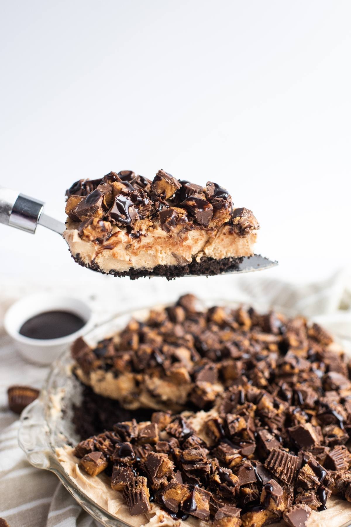 A slice of chocolate peanut butter cream pie topped with chopped candy and chocolate drizzle is being served.
