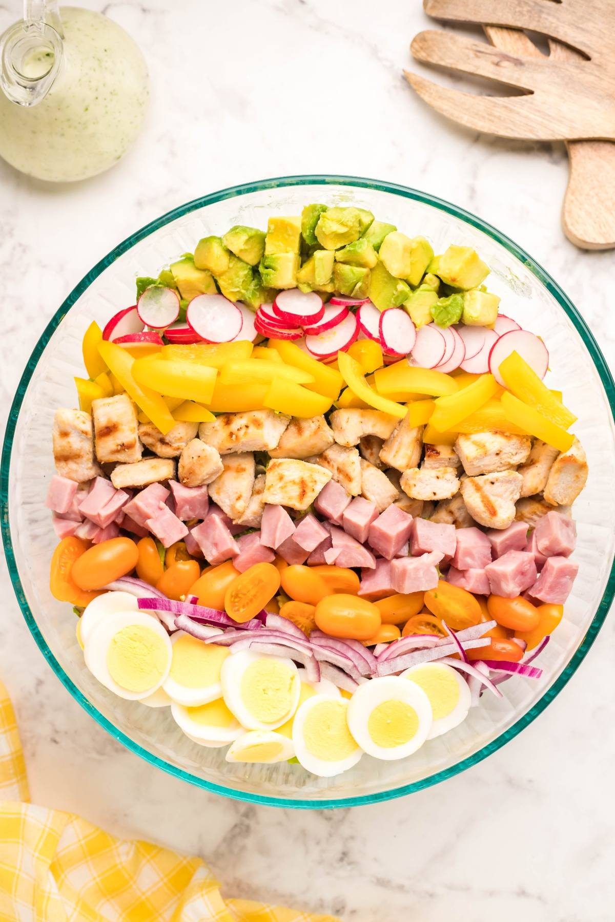 A vibrant Cobb salad bowl with rows of egg, onion, leftover ham, tomato, chicken, pepper, radish, and avocado on a marble surface—perfect with dairy free ranch dressing.