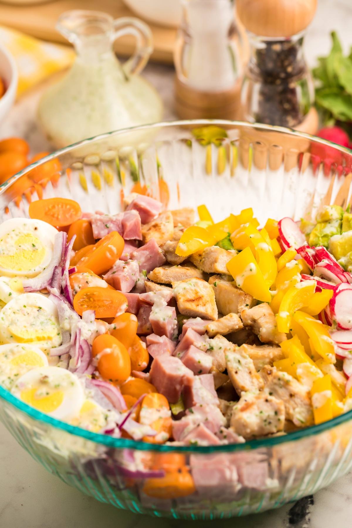 Glass bowl with chopped ham, chicken, eggs, cherry tomatoes, yellow peppers, and radishes arranged in rows for a filling dinner salad. Try it topped with dairy free ranch dressing for extra flavor.