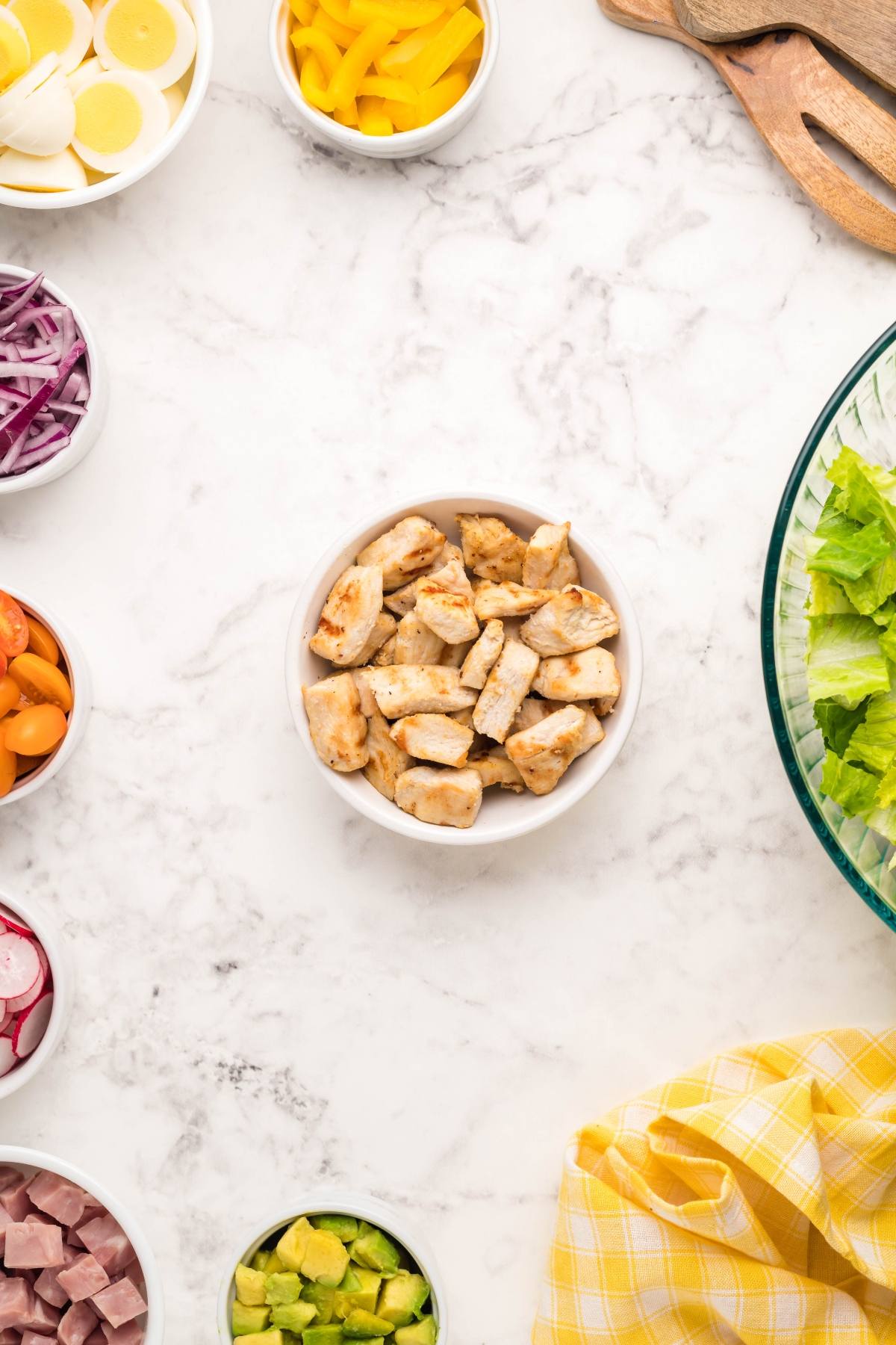 Bowl of grilled chicken surrounded by bowls of salad ingredients on a marble countertop—perfect for a filling dinner salad topped with dairy free ranch dressing.