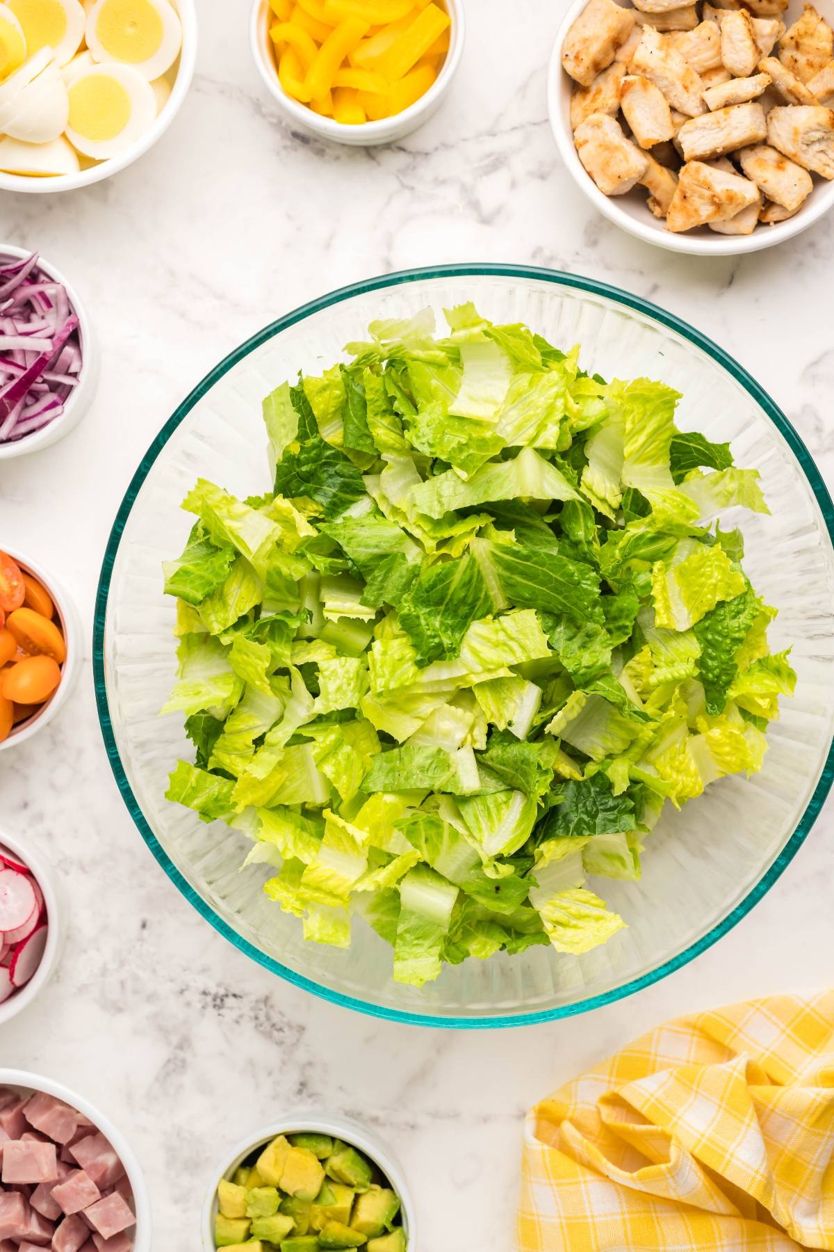 Bowl of chopped romaine lettuce surrounded by small bowls of salad toppings on a marble surface, perfect for creating a filling dinner salad with homemade ranch dressing.