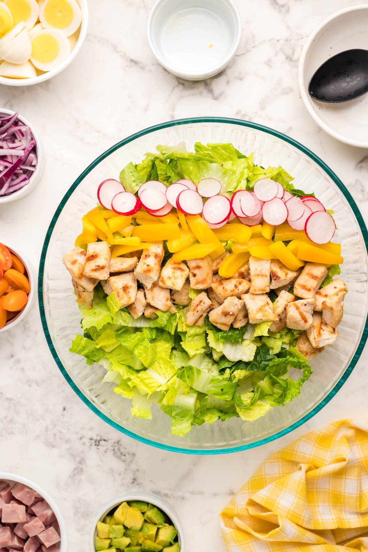 A filling dinner salad bowl with lettuce, grilled chicken, radish, yellow pepper, and small bowls of toppings—perfect when topped with dairy free ranch dressing.