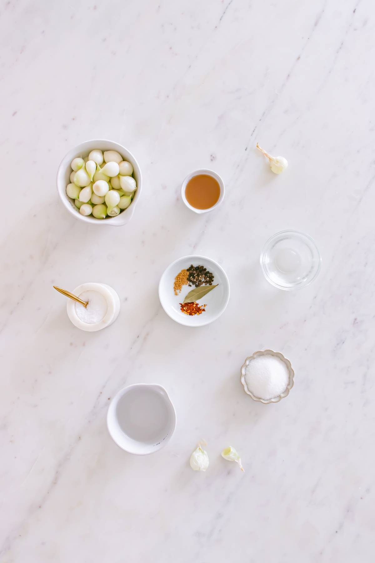 Ingredients for pickling arranged on a white marble surface, including onions, spices, salt, and liquids.