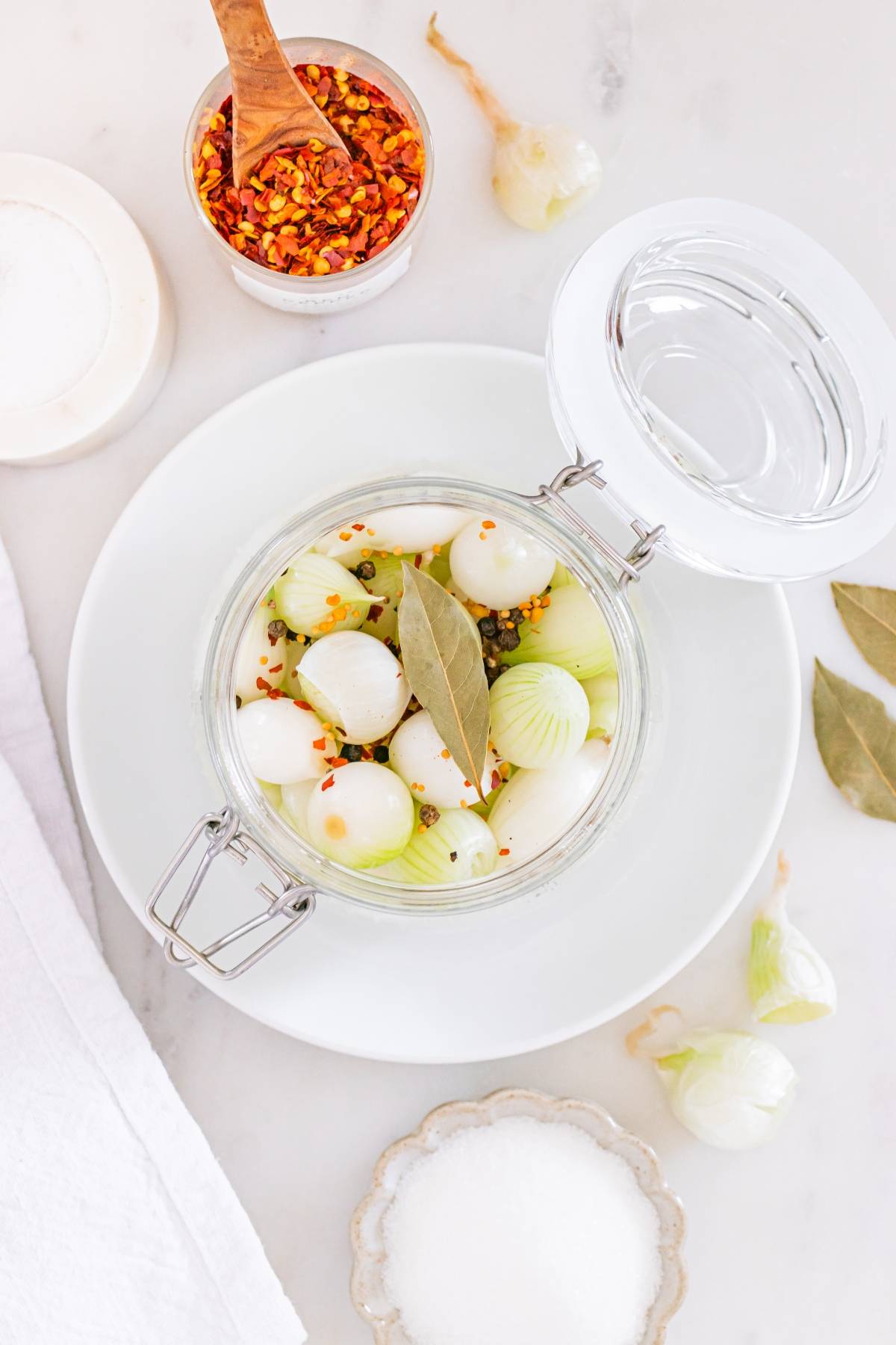 Glass jar filled with onions, bay leaf, and spices on a white plate, with seasonings on the side.