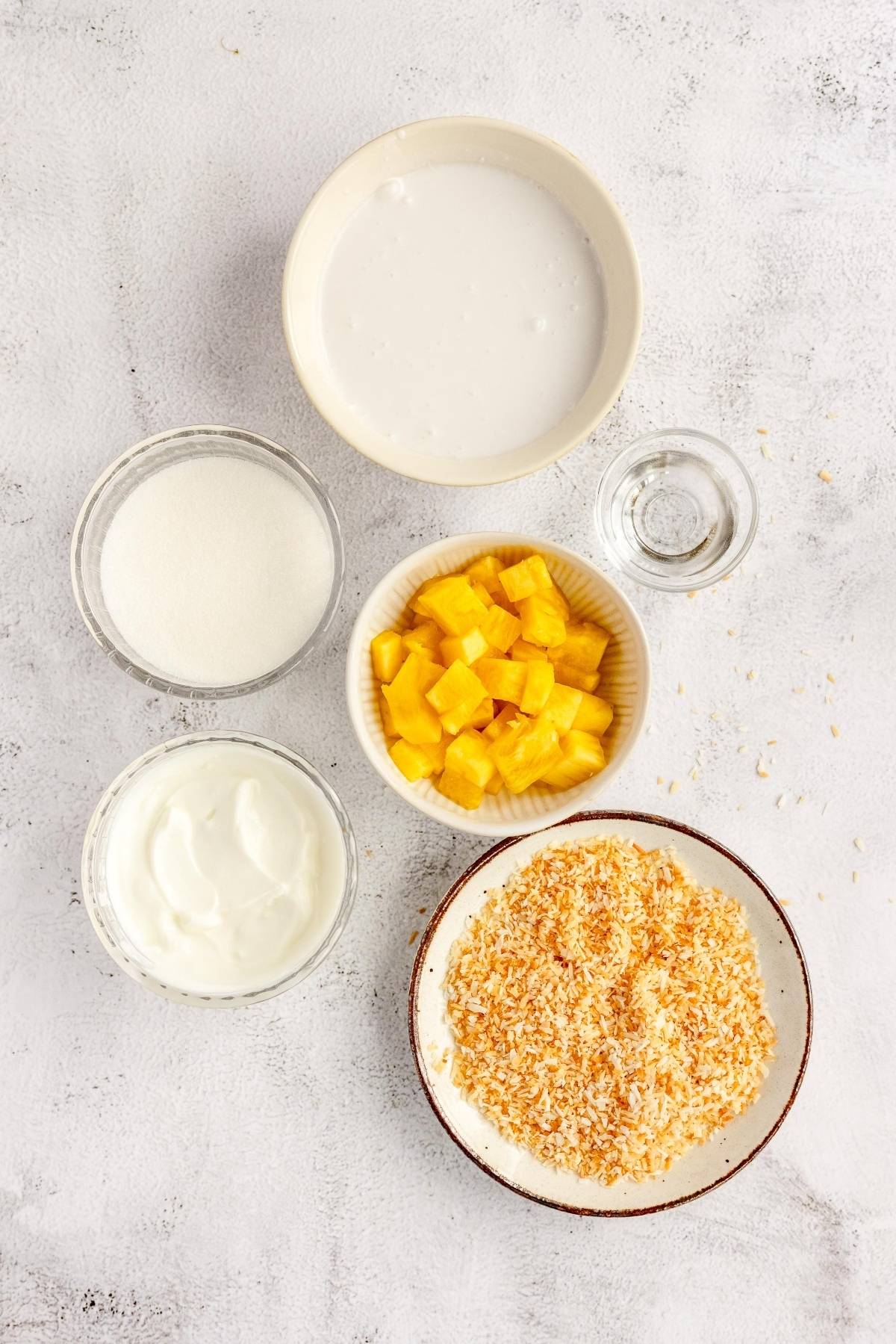 Five bowls featuring coconut cream, yogurt, sugar, diced mango, toasted coconut, and a small cup of clear liquid—perfect inspiration if you want to make froyo or try the best frozen yogurt recipe at home.