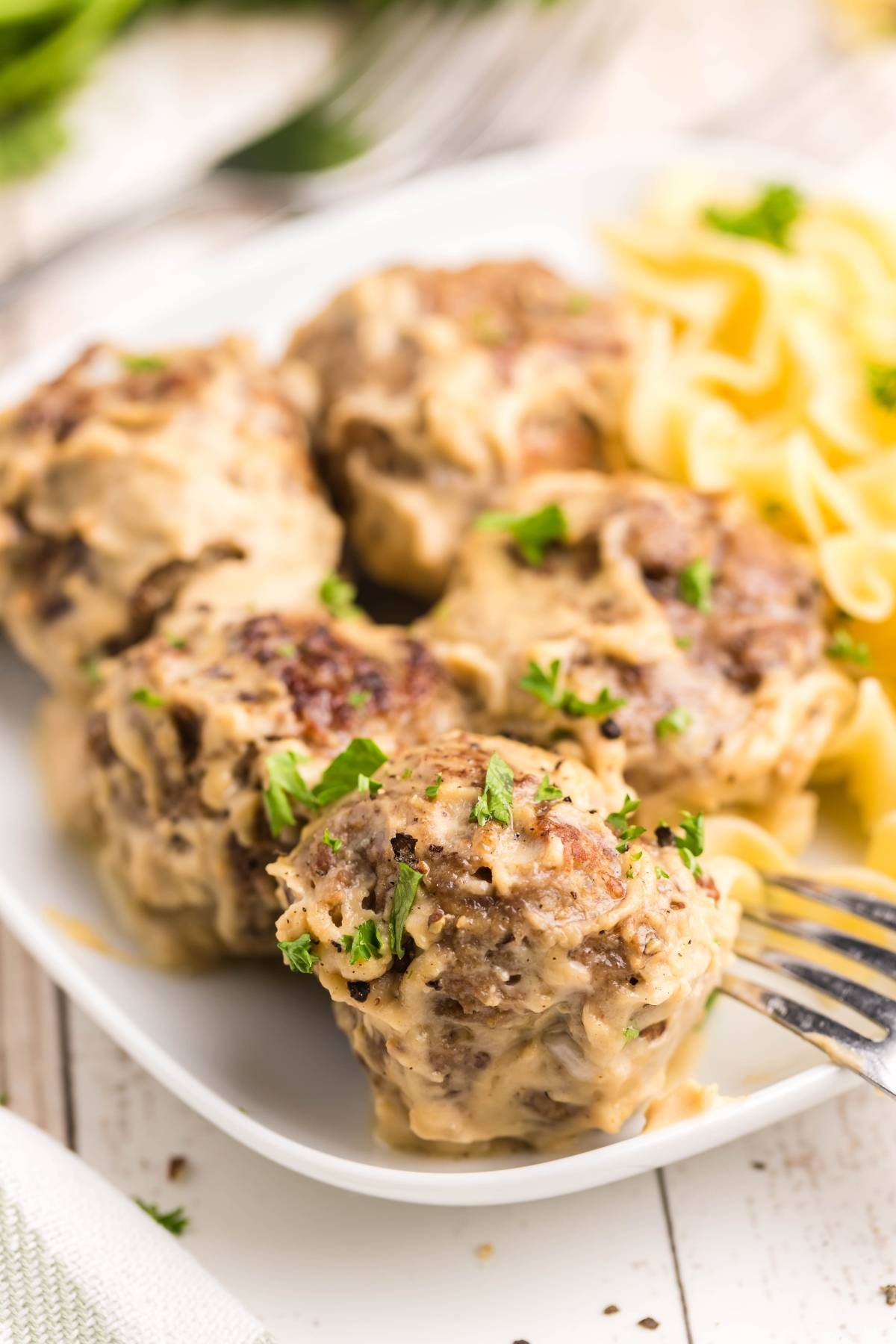 Four creamy Copycat Ikea Swedish meatballs, garnished with parsley and served with pasta on a white plate.