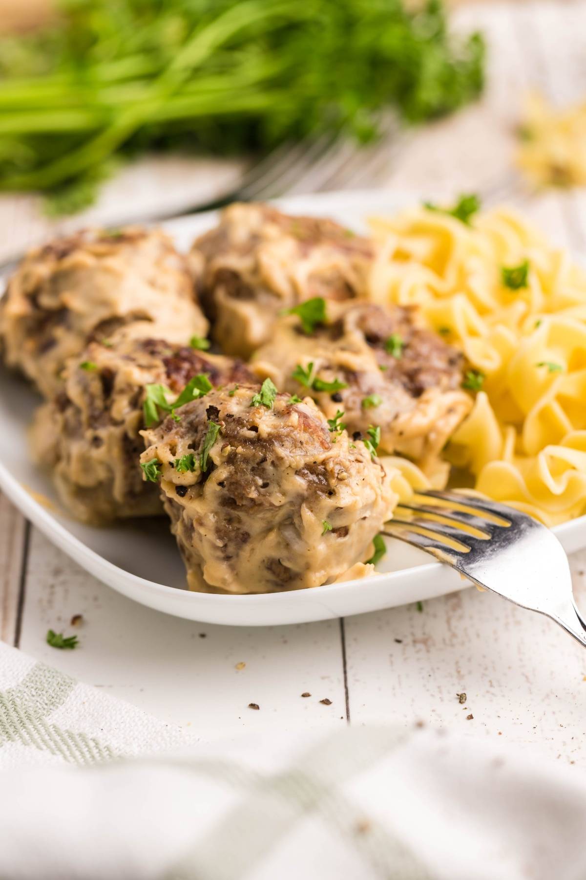 Meatballs with creamy sauce and parsley, served with egg noodles on a white plate—perfect for anyone searching for a copycat Ikea Swedish meatballs recipe.