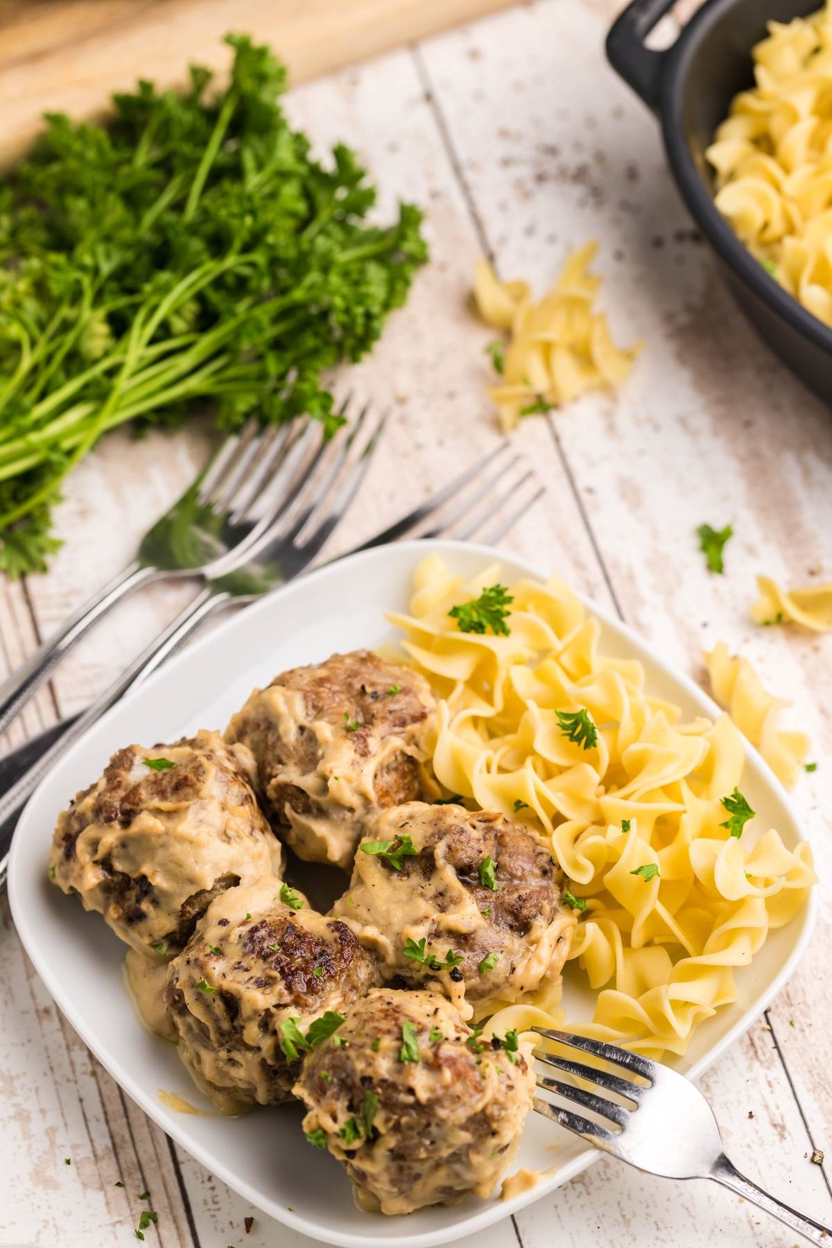 Four meatballs with creamy sauce and egg noodles on a white plate, garnished with parsley—just like the Copycat Ikea Swedish meatballs recipe.