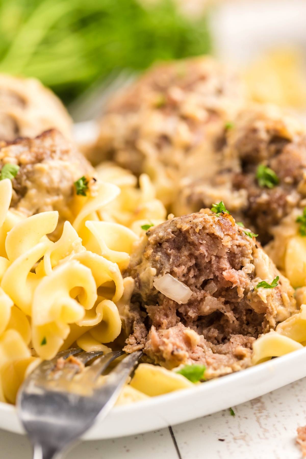 A plate of egg noodles and gluten free Swedish meatballs, with a fork and a meatball cut open to show the inside.