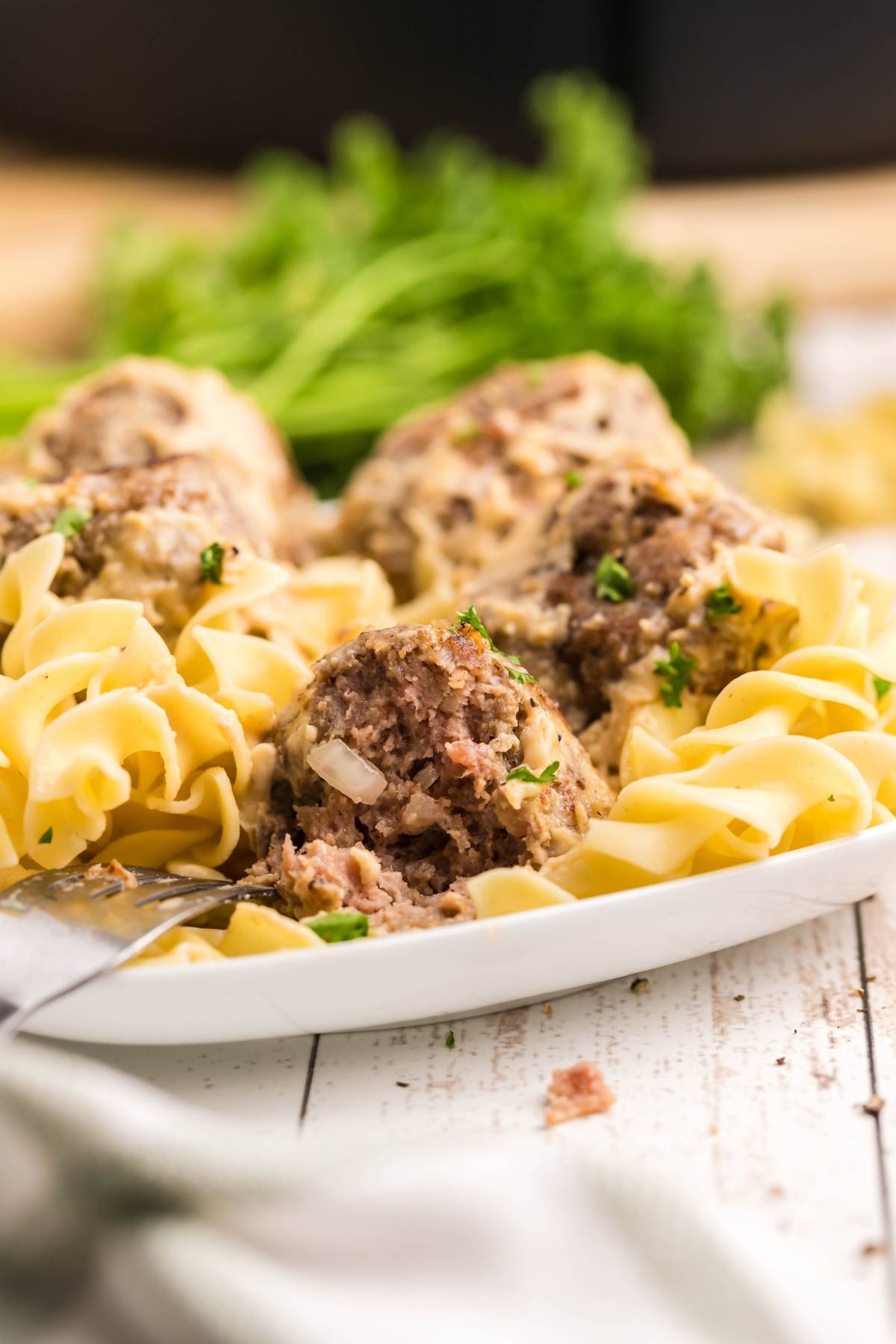 Plate of egg noodles with Copycat Ikea Swedish meatballs, garnished with parsley, on a white wooden table.