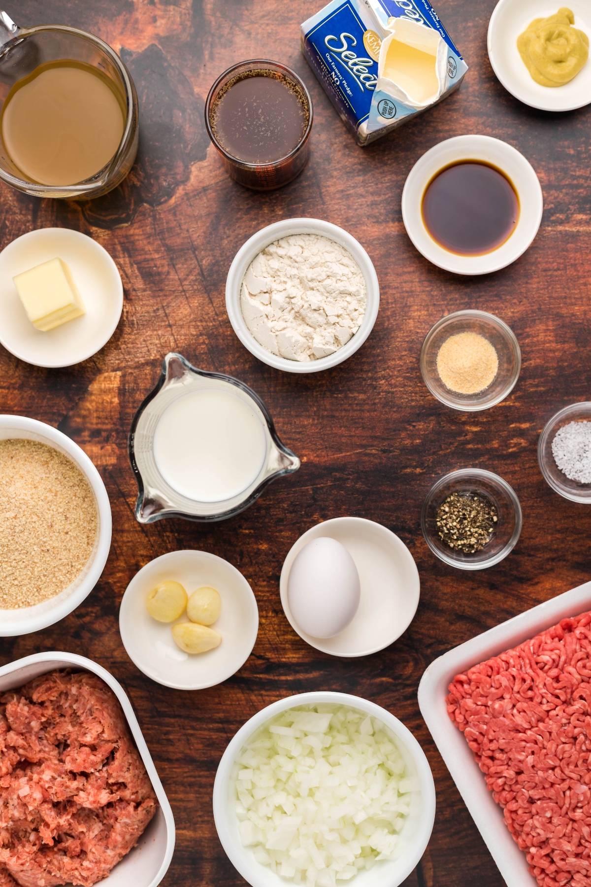 Ingredients for a Swedish meatball recipe, including ground beef, onion, milk, egg, seasonings, and sauces on a wooden surface.