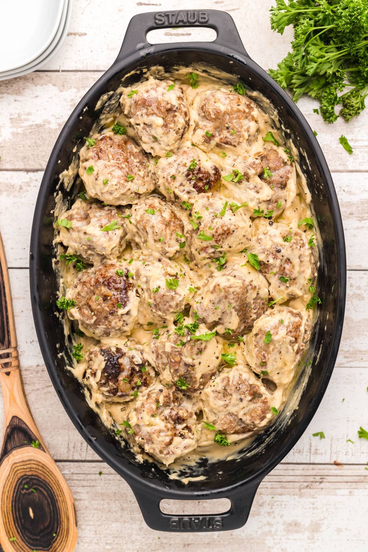 Meatballs in creamy sauce garnished with parsley in a black baking dish on a light wooden table—perfect for anyone searching for an authentic Swedish meatball recipe.