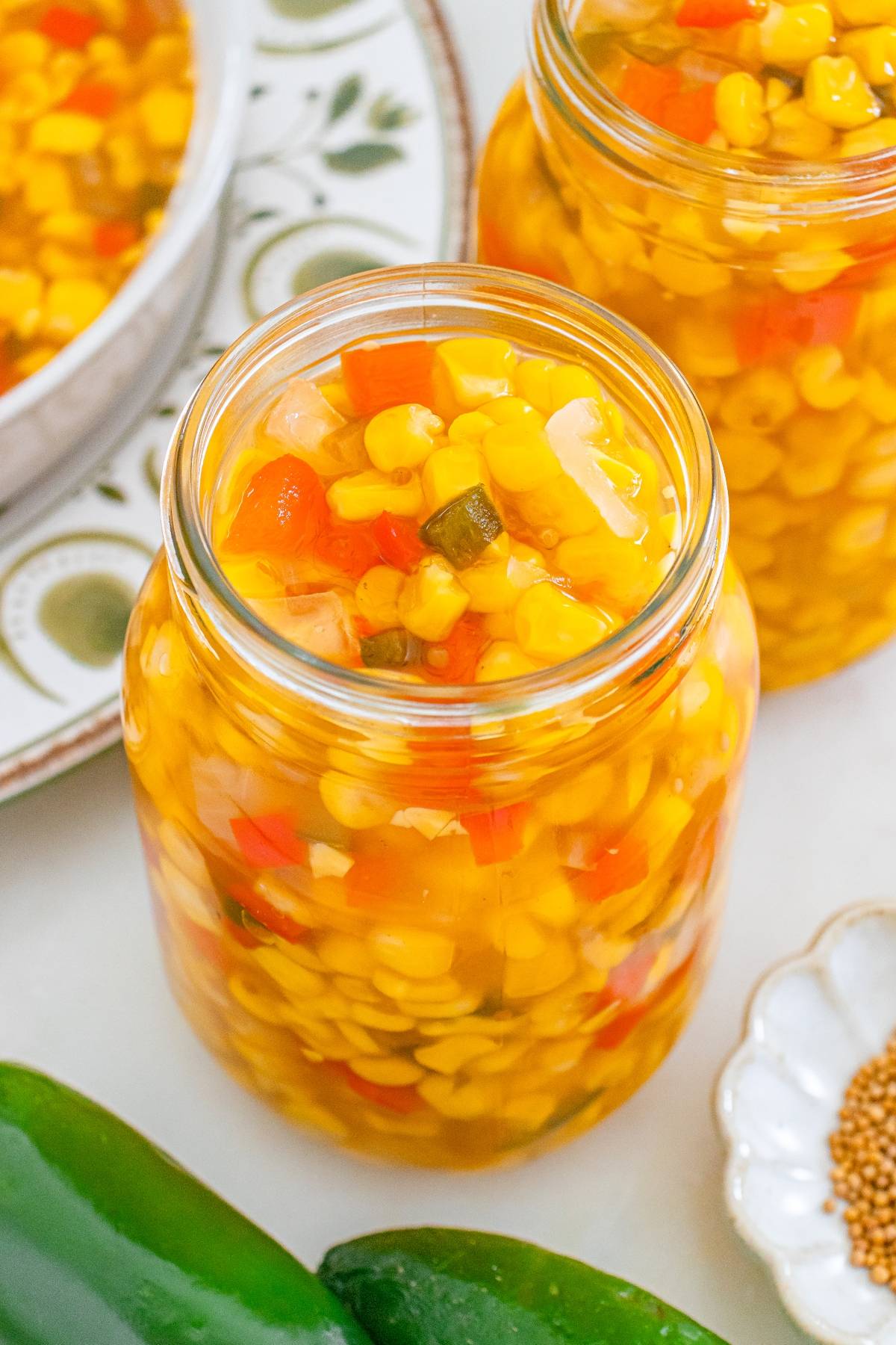 A jar filled with corn relish, featuring corn, red peppers, onions, and visible spices.