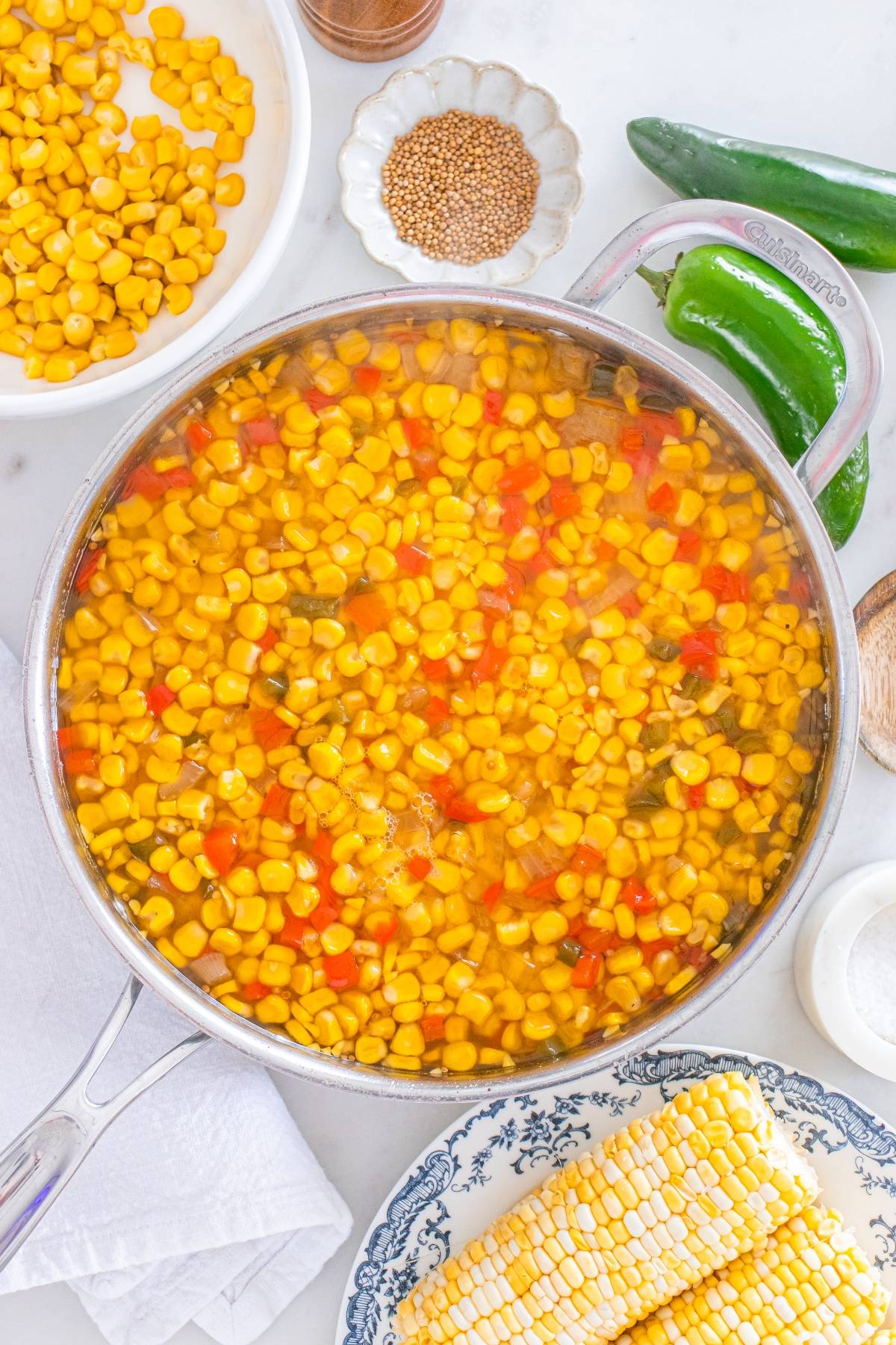 A pot of corn, diced red peppers, and jalapeños simmering in water, surrounded by fresh ingredients.