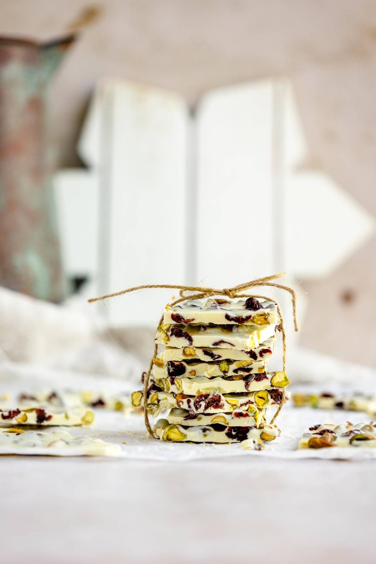 Stack of white chocolate bark with nuts and dried fruit, tied with twine, on a light surface—an easy holiday treat recipe for cranberry and pistachio lovers.