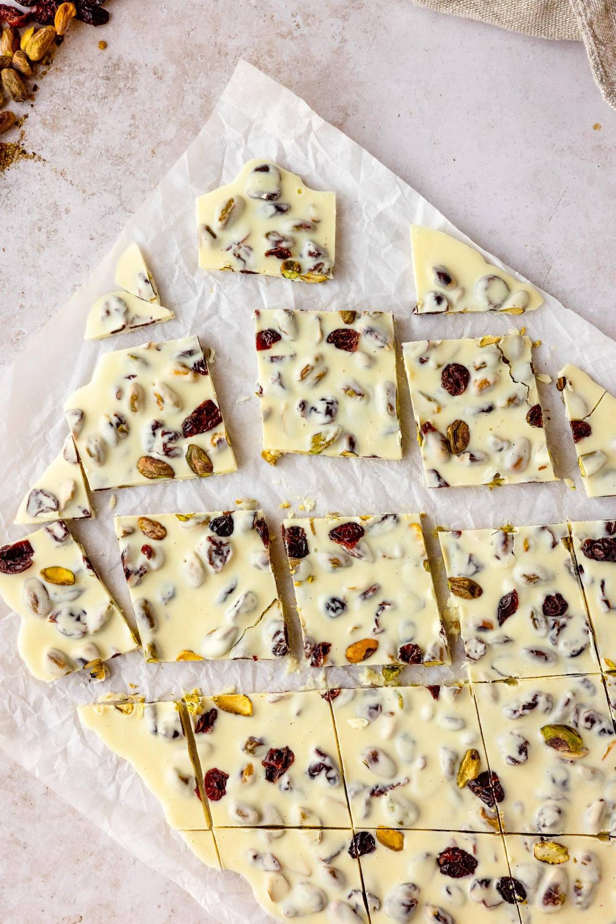 Cranberry Pistachio White Chocolate Bark with nuts and dried fruit, cut into squares on parchment paper—an easy holiday treat recipe using creamy white chocolate.