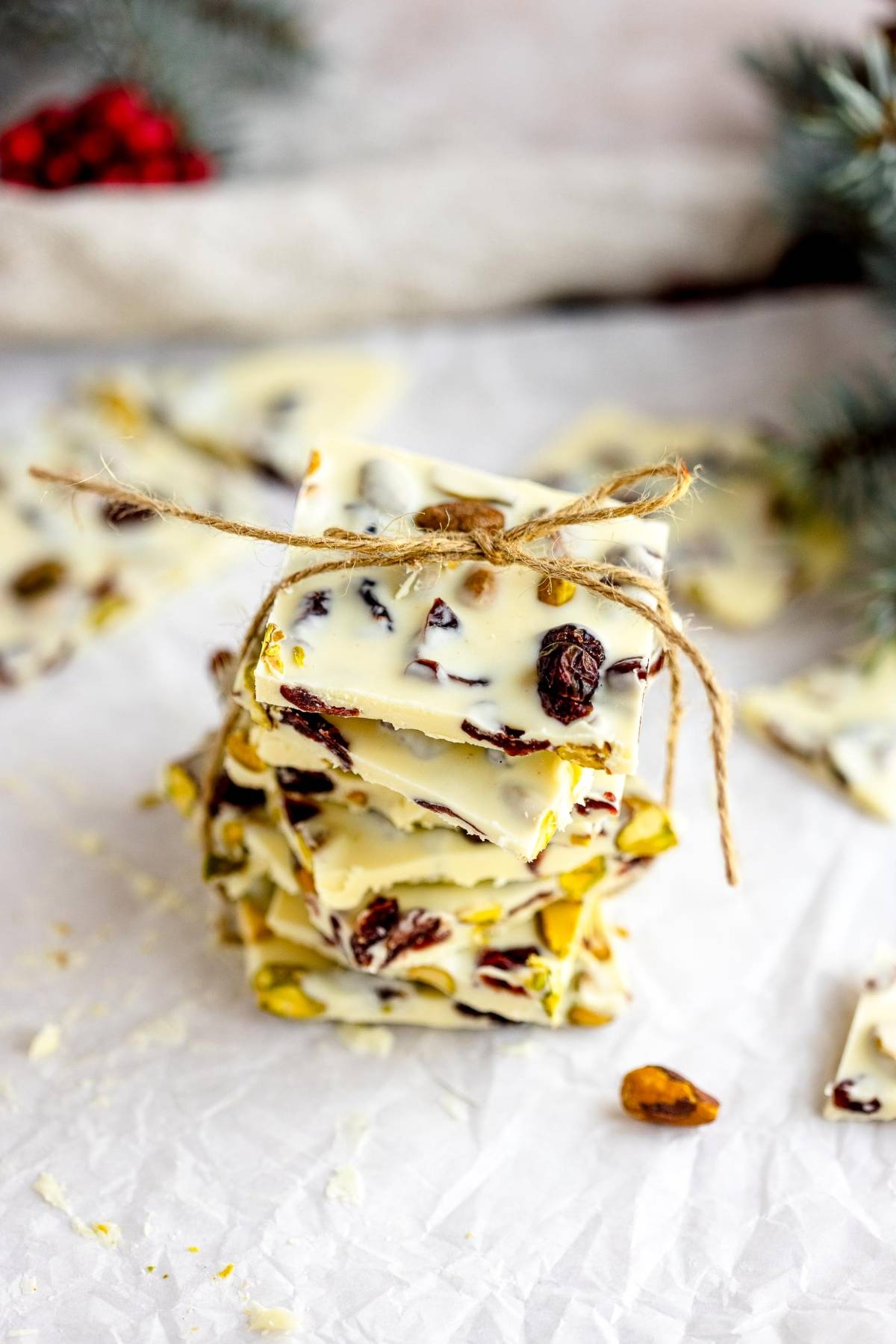 Stack of Cranberry Pistachio White Chocolate Bark with nuts and dried fruit, tied with twine, on a white surface.