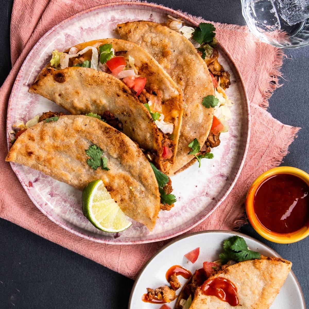 Three crispy tacos filled with veggies and savory ground turkey on a pink plate, served with lime, sauce, and cilantro—a quick and easy dinner inspired by our favorite turkey taco recipe.