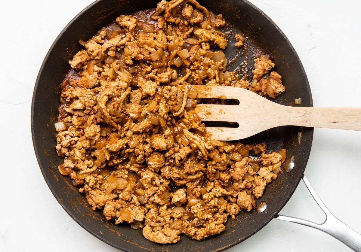 Cooked ground meat with onions and spices in a black skillet, stirred with a wooden spatula—perfect for crispy turkey tacos or as a quick and easy dinner recipe with ground turkey.