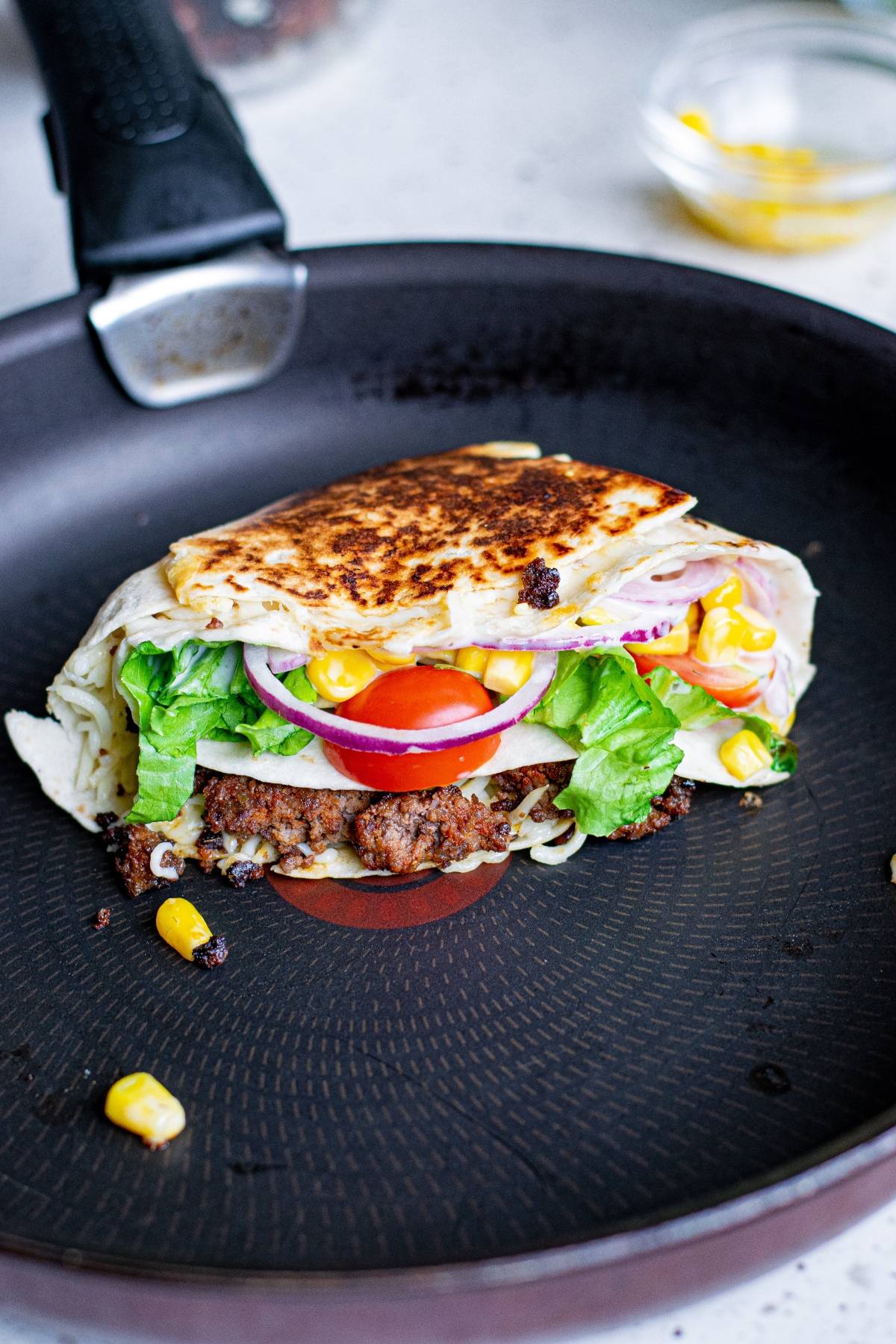 A grilled wrap inspired by the TikTok folded tortilla hack, packed with lettuce, tomato, onion, and corn sizzling in a non-stick skillet.