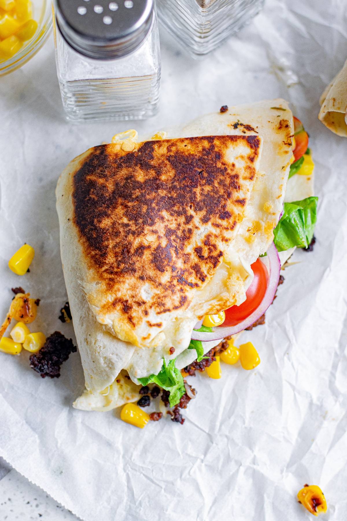 A crunchy beef tortilla folded wrap, filled with lettuce, tomato, onion, ground beef, and corn sits on parchment paper—perfect for trying the viral folded tortilla hack.
