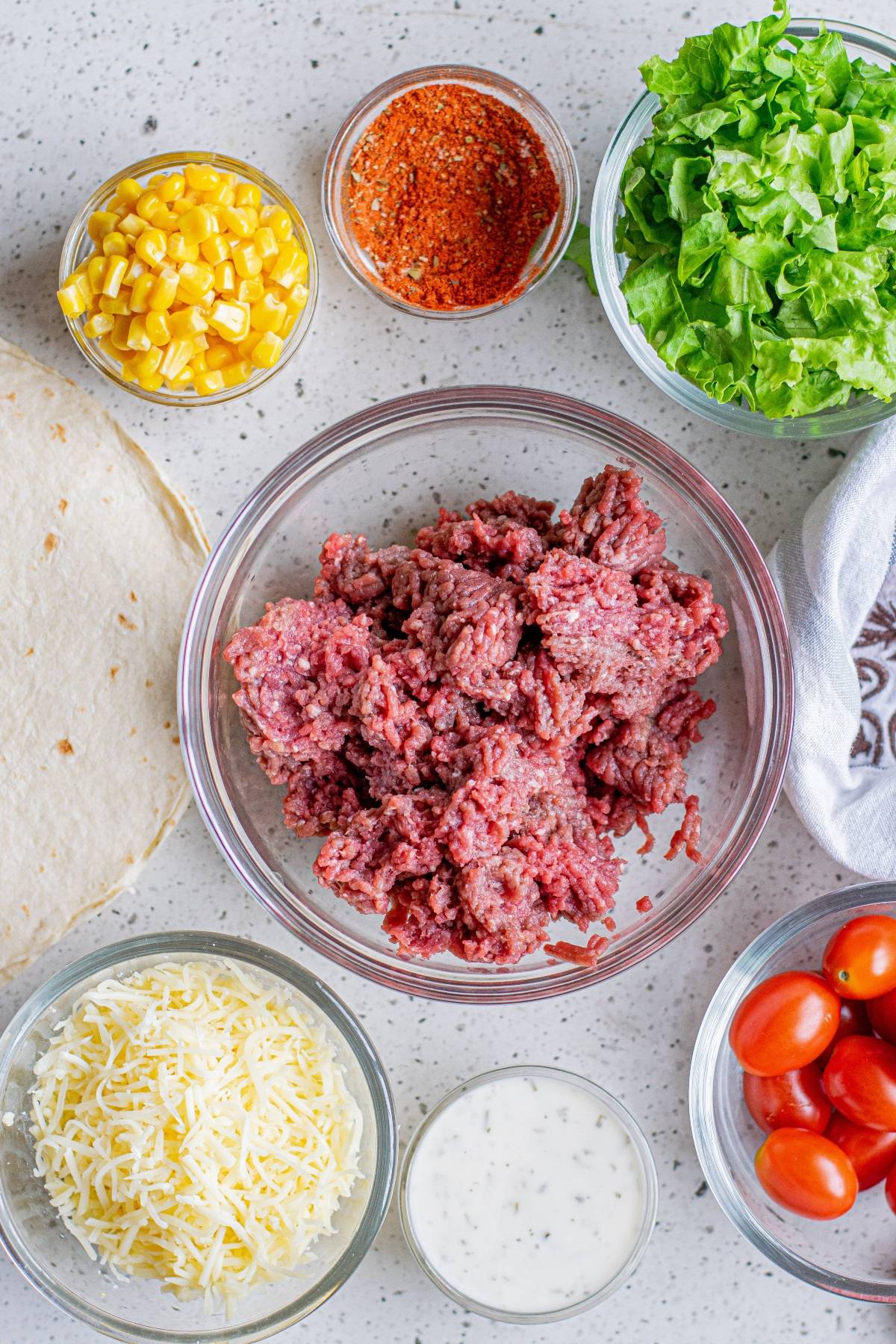Taco ingredients: ground beef, shredded cheese, ranch, cherry tomatoes, lettuce, corn, tortillas, and taco seasoning—perfect for making the viral TikTok tortilla folded wrap or your own crunchy beef tortilla folded hack.