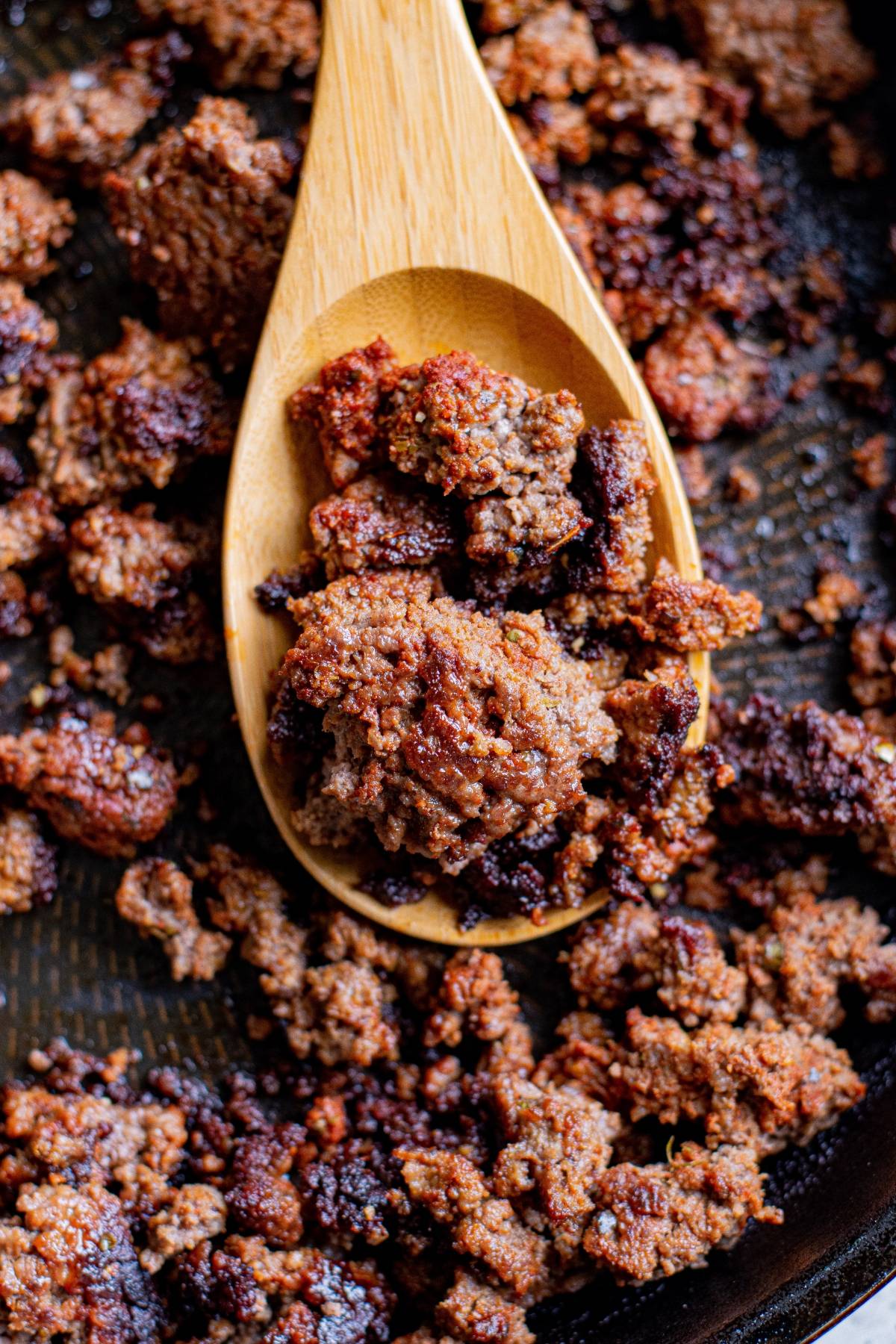 Cooked and browned ground beef in a skillet, perfect for making a crunchy beef tortilla, with a wooden spoon scooping some of the meat.