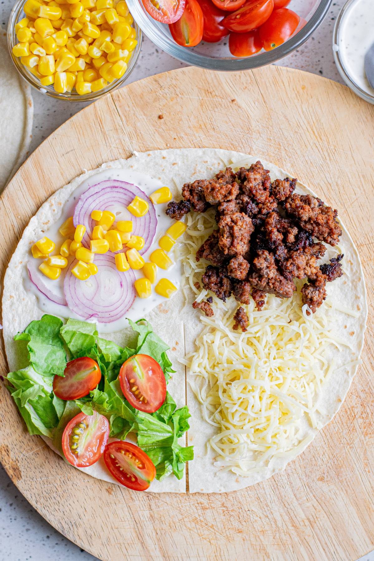A Crunchy beef tortilla with ground beef, shredded cheese, lettuce, tomato, onion, and corn served on a wooden board.